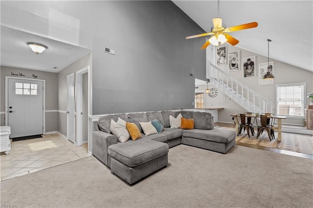 living area with visible vents, stairway, light carpet, light tile patterned floors, and high vaulted ceiling