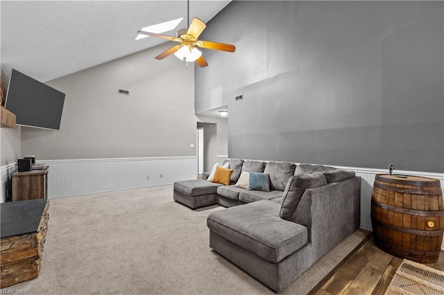 carpeted living area with a wainscoted wall, high vaulted ceiling, visible vents, and ceiling fan