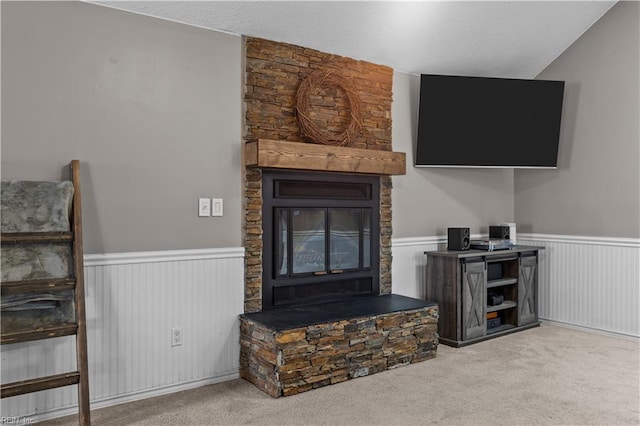 carpeted living room with a stone fireplace and wainscoting