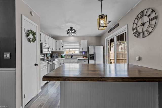 kitchen featuring wooden counters, a peninsula, a sink, stainless steel appliances, and white cabinets