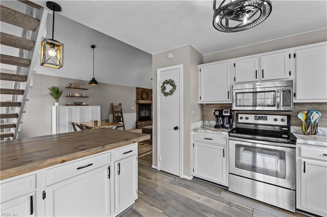 kitchen with wood finished floors, stainless steel appliances, hanging light fixtures, white cabinetry, and butcher block counters