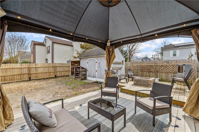 wooden deck with an outbuilding, a shed, an outdoor living space with a fire pit, and a fenced backyard