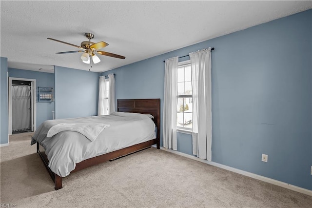 carpeted bedroom with a textured ceiling, baseboards, and a ceiling fan