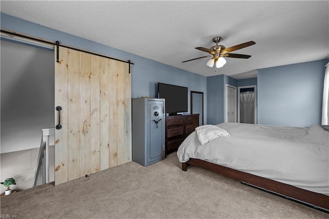 carpeted bedroom featuring ceiling fan, a barn door, and a textured ceiling