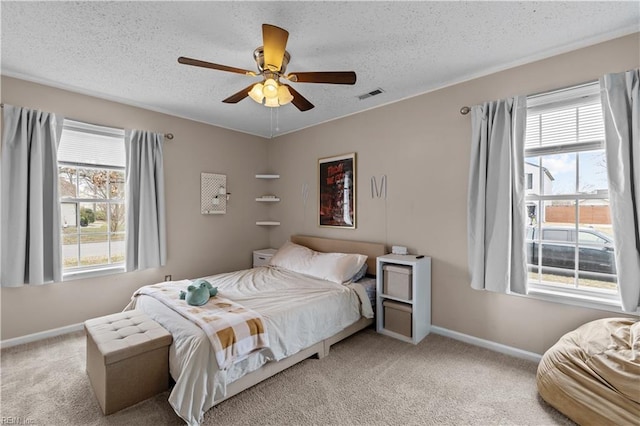 bedroom with a ceiling fan, visible vents, baseboards, a textured ceiling, and light carpet