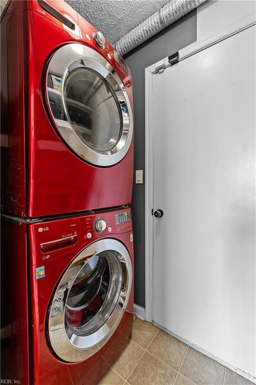 laundry room featuring laundry area, stacked washer and clothes dryer, tile patterned floors, and a textured ceiling