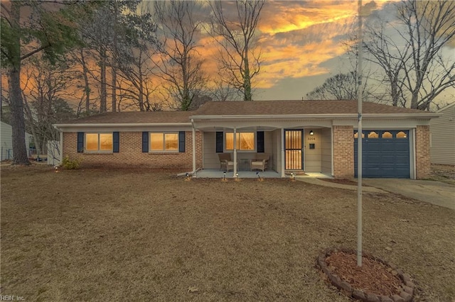 single story home with driveway, brick siding, covered porch, and an attached garage