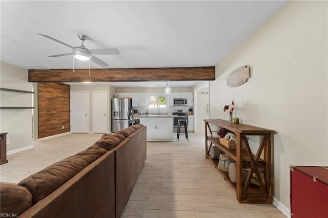 living area featuring light wood-style flooring, baseboards, beamed ceiling, and ceiling fan