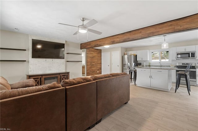 living area with a ceiling fan, beamed ceiling, and light wood-style floors