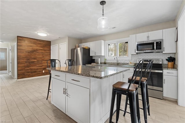 kitchen with backsplash, a kitchen island, stainless steel appliances, wooden walls, and a breakfast bar area