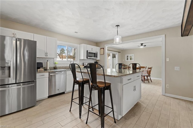 kitchen featuring a kitchen island, a breakfast bar, stainless steel appliances, decorative backsplash, and white cabinetry