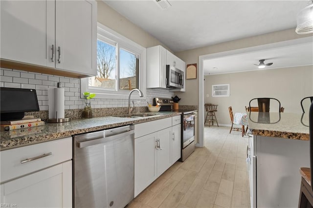 kitchen featuring a sink, tasteful backsplash, stainless steel appliances, white cabinets, and stone counters