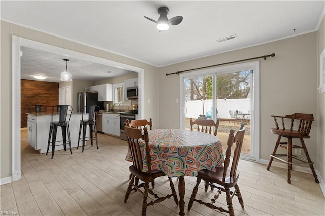 dining room featuring visible vents, light wood-style flooring, ornamental molding, baseboards, and ceiling fan