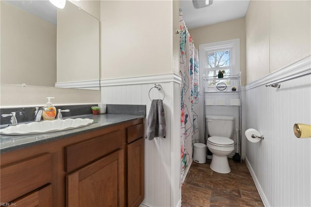 full bath with a wainscoted wall, toilet, vanity, and a shower with curtain