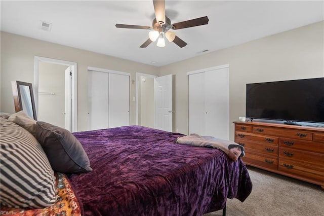 carpeted bedroom with visible vents, two closets, and a ceiling fan