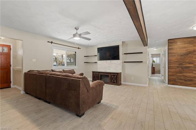 living area with a wealth of natural light, a glass covered fireplace, light wood-style flooring, and a ceiling fan