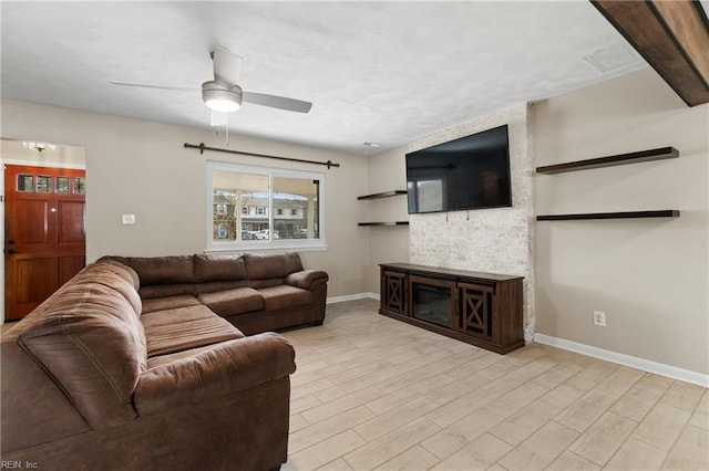 living area with a ceiling fan, light wood-style flooring, a fireplace, and baseboards