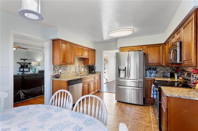 kitchen featuring a sink, light stone counters, appliances with stainless steel finishes, brown cabinetry, and decorative backsplash