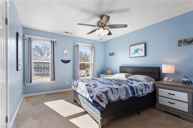 carpeted bedroom with visible vents, multiple windows, baseboards, and ceiling fan