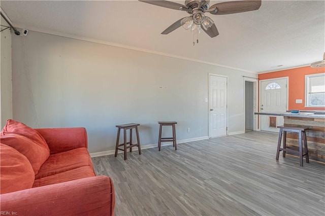 living area with a textured ceiling, wood finished floors, crown molding, baseboards, and ceiling fan