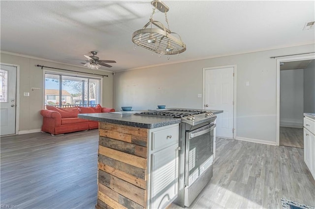 kitchen with stainless steel gas range oven, white cabinets, light wood-type flooring, and baseboards