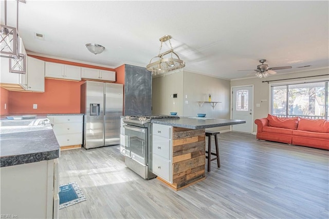 kitchen with dark countertops, white cabinets, appliances with stainless steel finishes, and light wood-type flooring