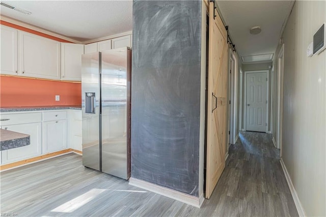 interior space with a barn door, light wood-style floors, visible vents, and baseboards