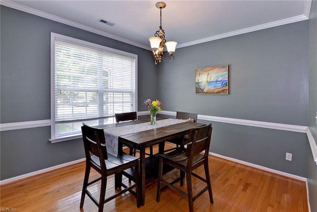 dining area with light wood-type flooring, visible vents, a notable chandelier, crown molding, and baseboards