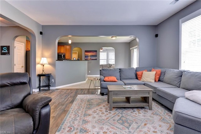 living room with wood finished floors, arched walkways, and baseboards