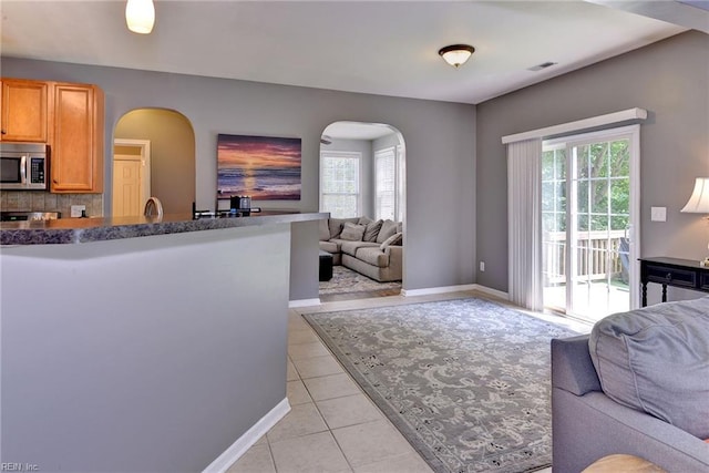 kitchen with stainless steel microwave, dark countertops, open floor plan, arched walkways, and light tile patterned flooring