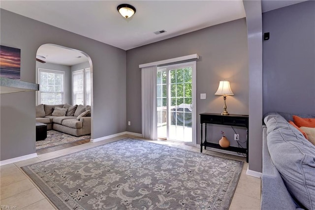 tiled living room featuring visible vents, arched walkways, and baseboards