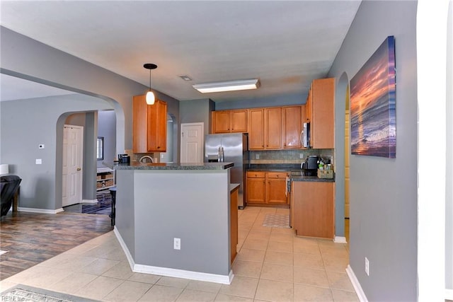 kitchen featuring dark countertops, arched walkways, appliances with stainless steel finishes, a peninsula, and light tile patterned floors