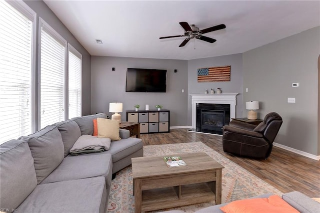 living area with wood finished floors, baseboards, visible vents, ceiling fan, and a glass covered fireplace