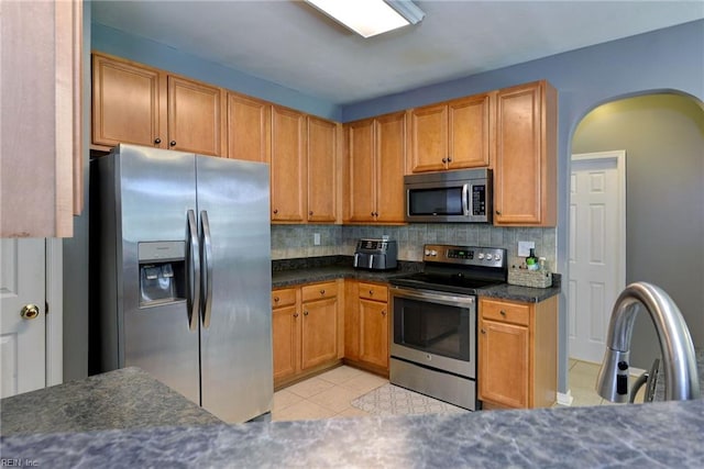 kitchen featuring light tile patterned floors, arched walkways, backsplash, and stainless steel appliances