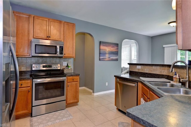 kitchen with tasteful backsplash, dark countertops, appliances with stainless steel finishes, arched walkways, and a sink