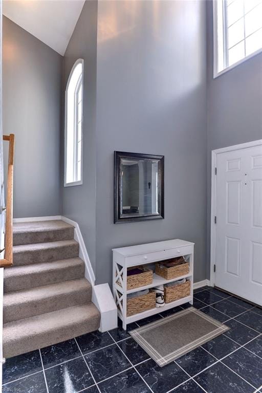 foyer featuring baseboards, high vaulted ceiling, a healthy amount of sunlight, and stairs