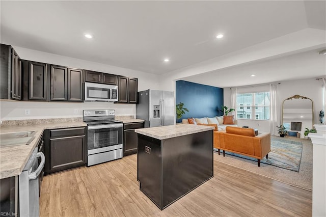 kitchen with light wood finished floors, a kitchen island, light countertops, appliances with stainless steel finishes, and open floor plan