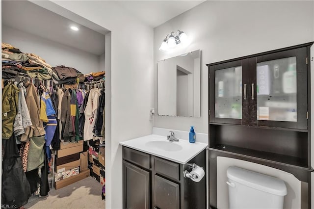 bathroom with a walk in closet, toilet, and vanity