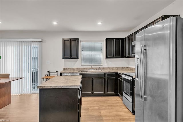 kitchen featuring light wood finished floors, a kitchen island, a sink, light countertops, and appliances with stainless steel finishes