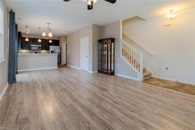 unfurnished living room with stairway, a ceiling fan, baseboards, and light wood finished floors