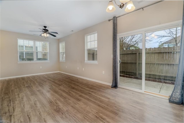 spare room featuring ceiling fan with notable chandelier, baseboards, and wood finished floors