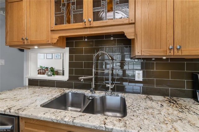 kitchen featuring light stone counters, backsplash, glass insert cabinets, and a sink