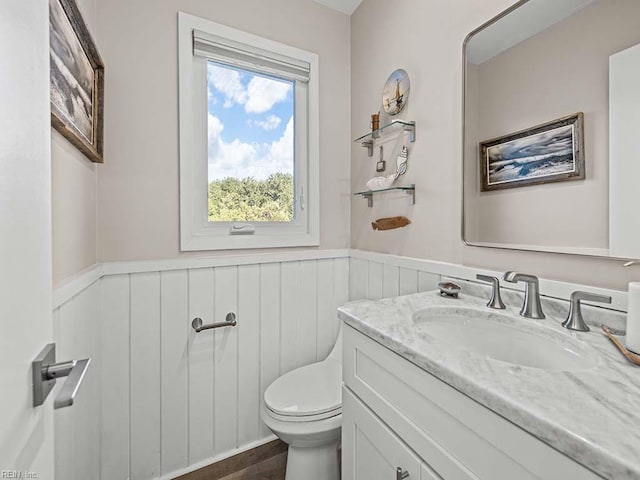 half bathroom with vanity, toilet, and wainscoting