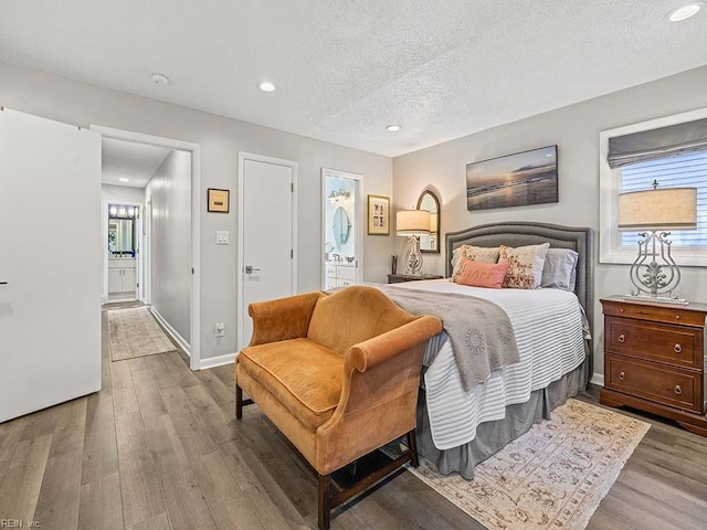 bedroom featuring connected bathroom, baseboards, a textured ceiling, and wood finished floors