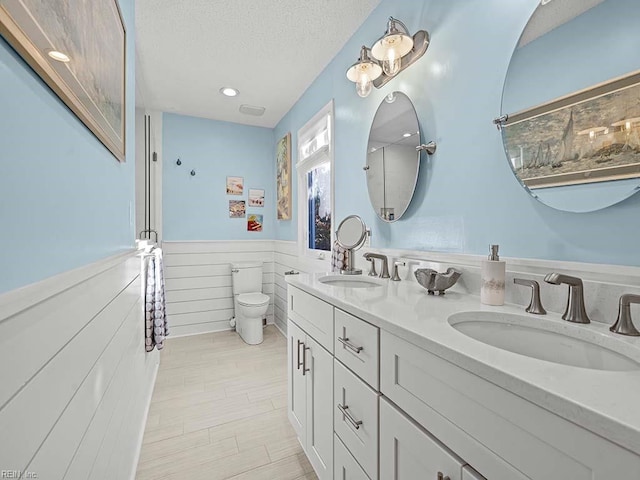 full bath featuring wainscoting, a textured ceiling, toilet, and a sink