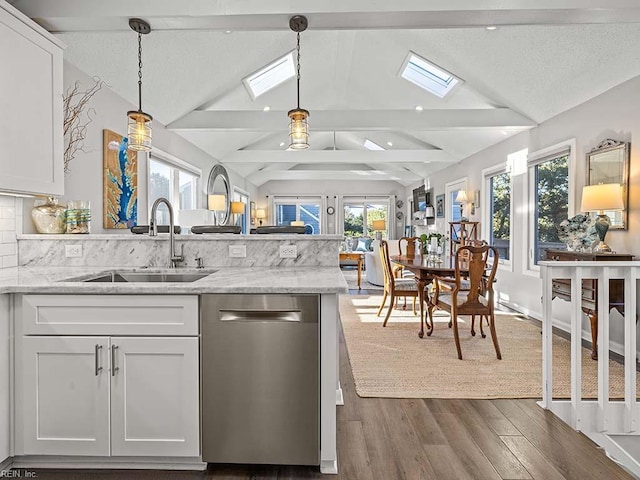 kitchen with dishwasher, lofted ceiling with skylight, white cabinetry, and a sink