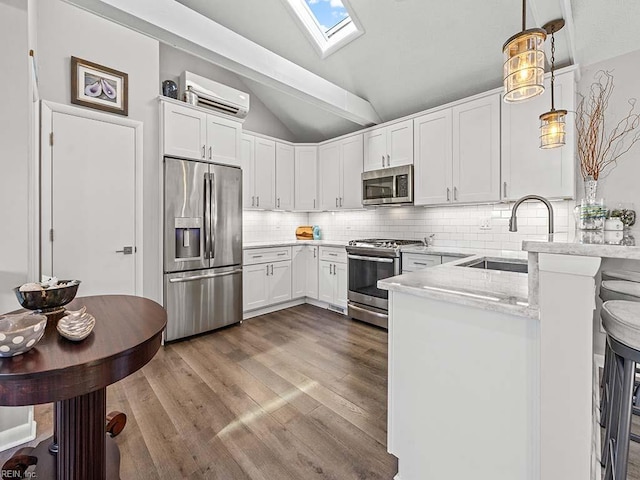 kitchen with an AC wall unit, a sink, vaulted ceiling with skylight, appliances with stainless steel finishes, and a peninsula