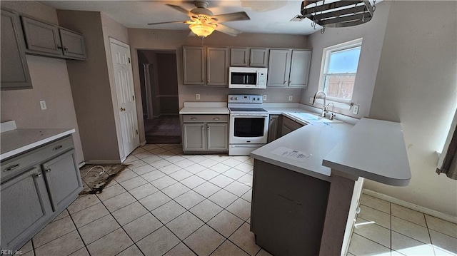 kitchen with white microwave, a peninsula, gray cabinets, a sink, and range with electric cooktop