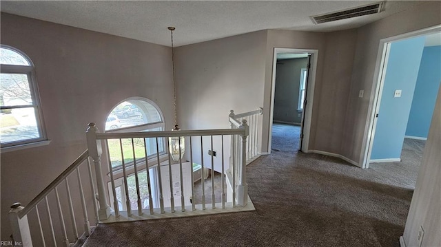 hallway with visible vents, baseboards, carpet floors, an upstairs landing, and a textured ceiling