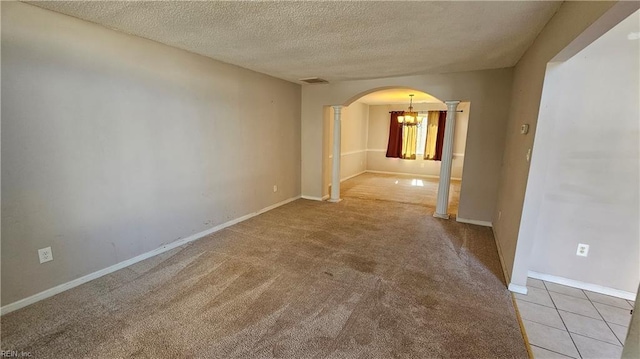 spare room with visible vents, light colored carpet, decorative columns, arched walkways, and a textured ceiling